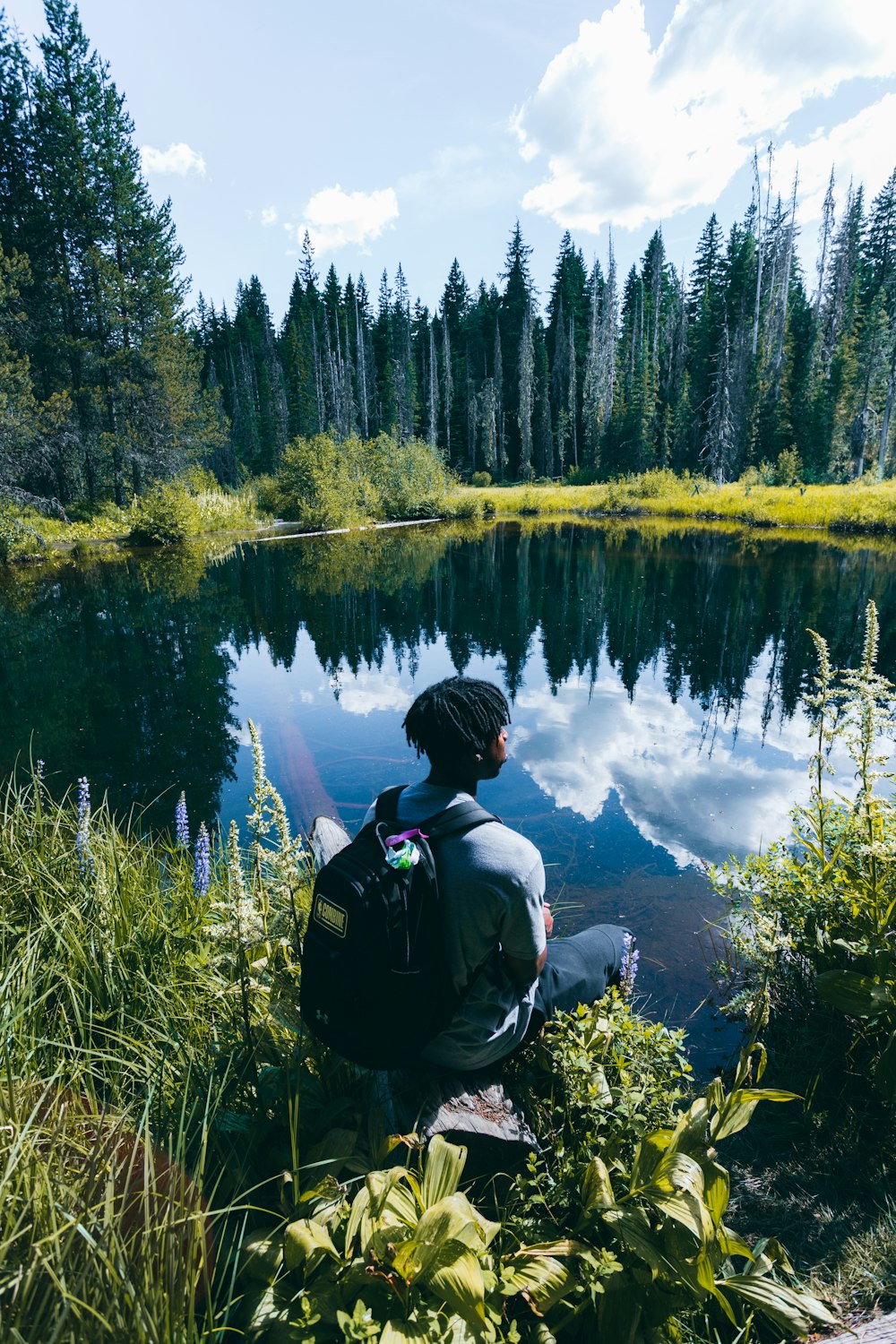 man in black jacket and black backpack standing on green grass field near lake during daytime