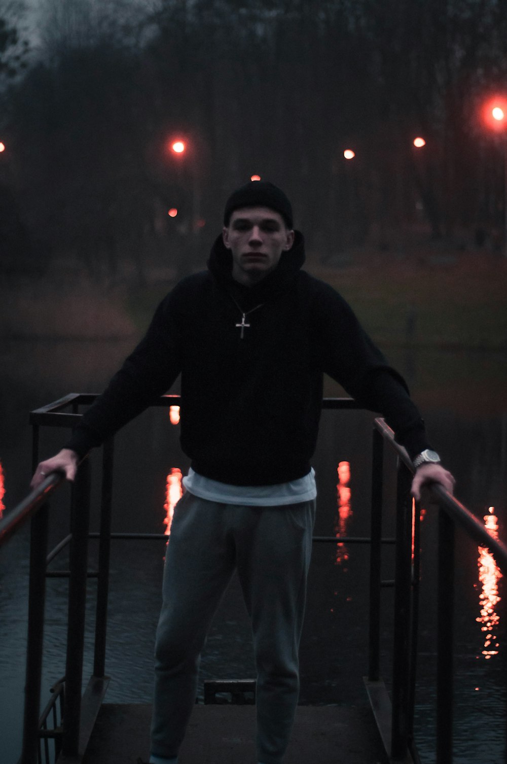 man in black hoodie and gray pants standing on black steel fence during nighttime