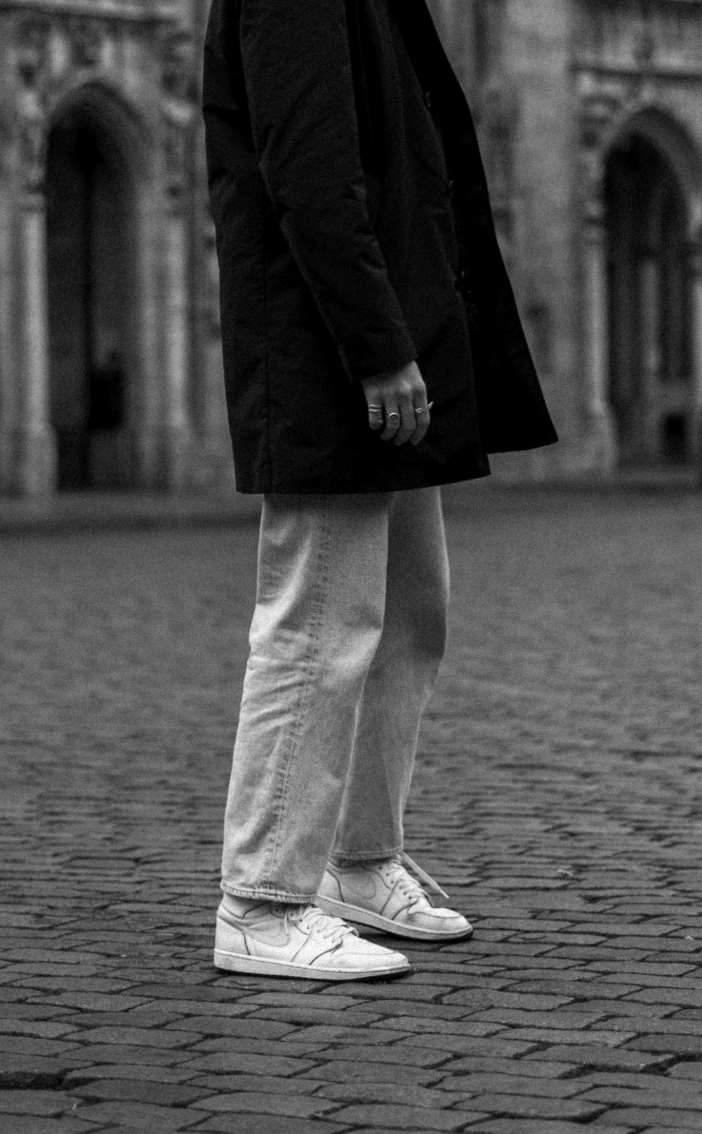 person in black coat and white pants standing on gray concrete floor