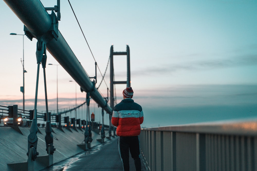 person in red jacket and black pants standing on gray concrete road during daytime