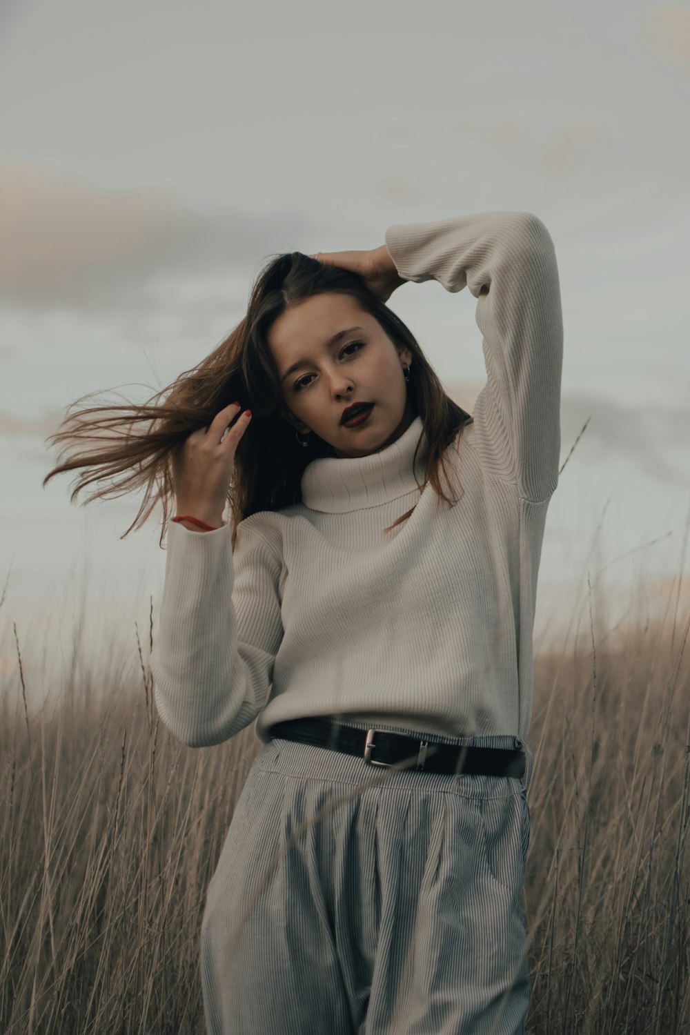 Femme en pull à col roulé blanc et jean en denim gris debout sur un champ d’herbe brune pendant la journée