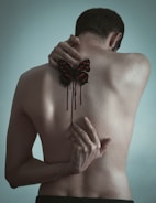 A person is depicted from the back, with a black and red butterfly tattoo on their skin. The tattoo appears to be bleeding, with red streaks dripping down.