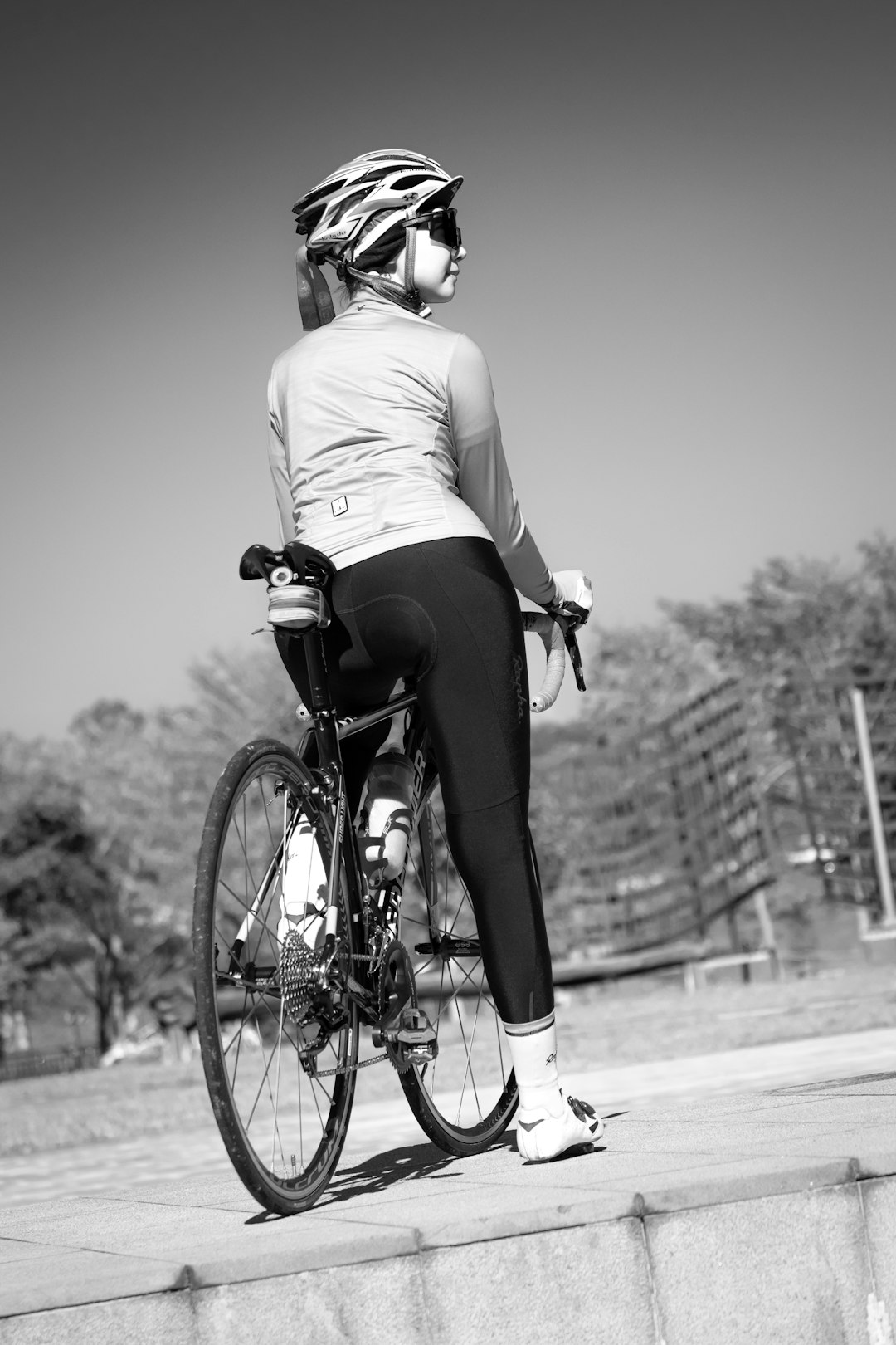 grayscale photo of woman in white shirt and black shorts riding on bicycle