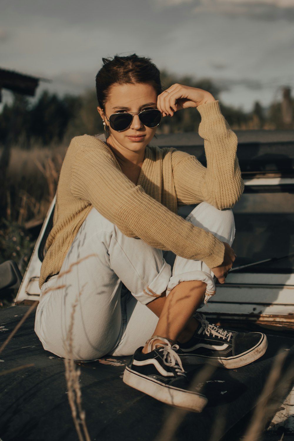 woman in brown sweater and white pants wearing black sunglasses sitting on brown wooden bench during