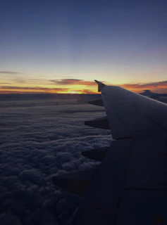 A vibrant sunset view from an airplane window, showing the wing and clouds below.