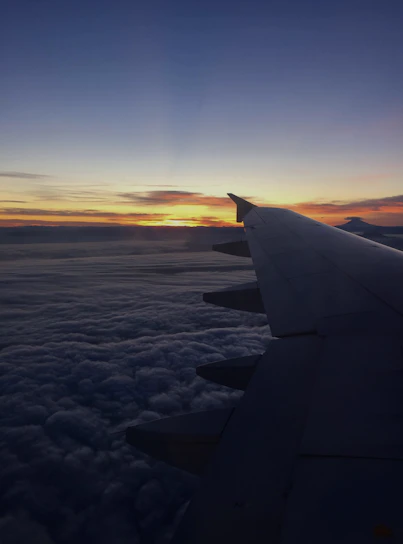 A vibrant sunset view from an airplane window, showing the wing and clouds below.