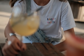 woman in white crew neck t-shirt holding clear drinking glass