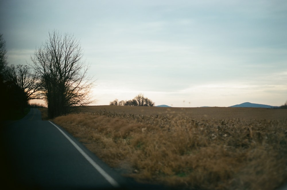 black asphalt road between brown grass field during daytime