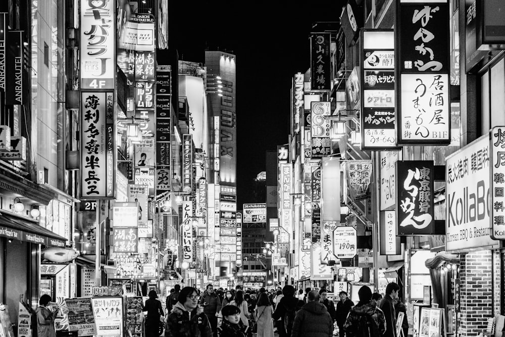 grayscale photo of people walking on street between high rise buildings