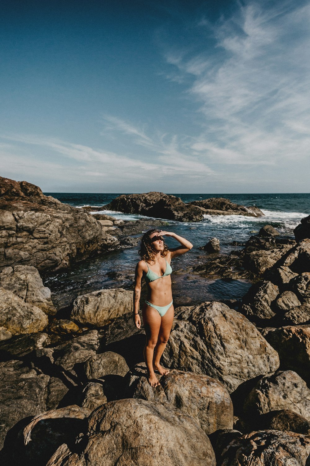 woman in black bikini standing on rocky shore during daytime