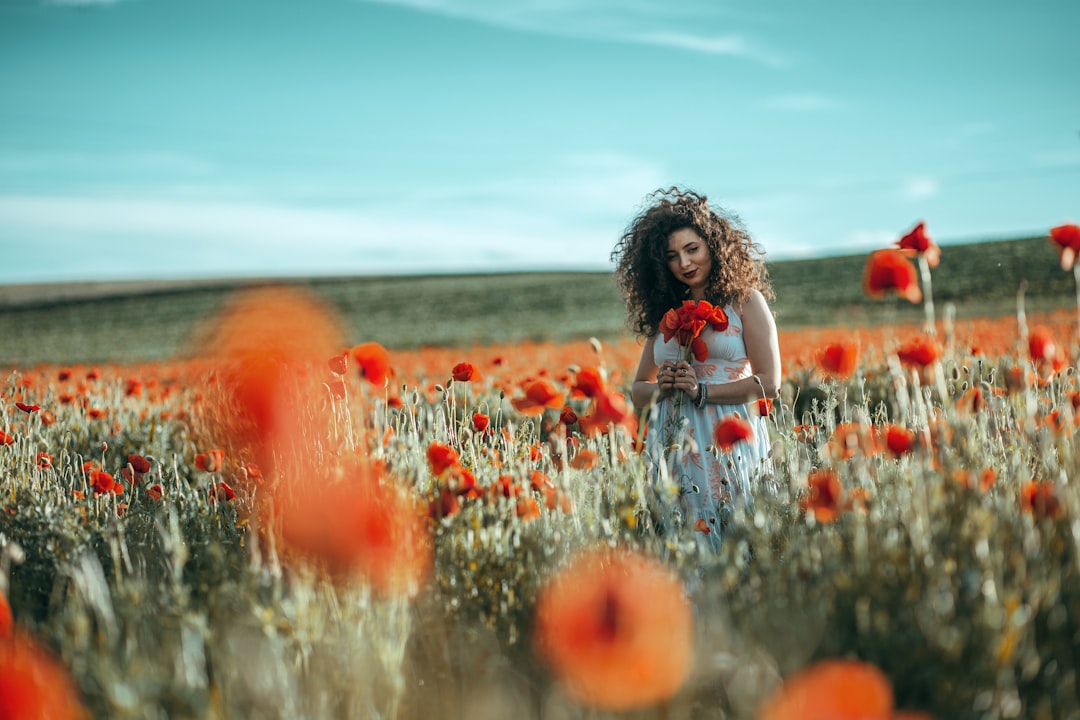 girl in white shirt sitting on red flower field during daytime