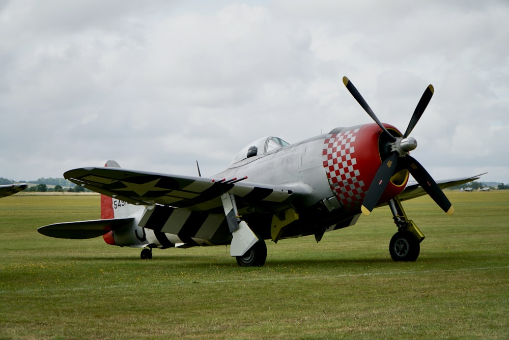 red and gray fighter plane on green grass field under white clouds during daytime
