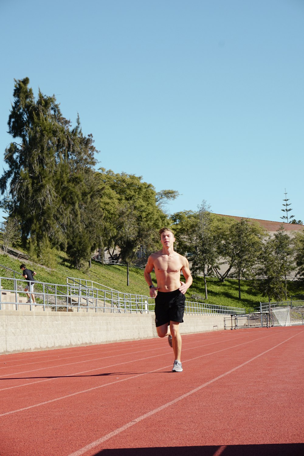 topless man in black shorts running on track field during daytime
