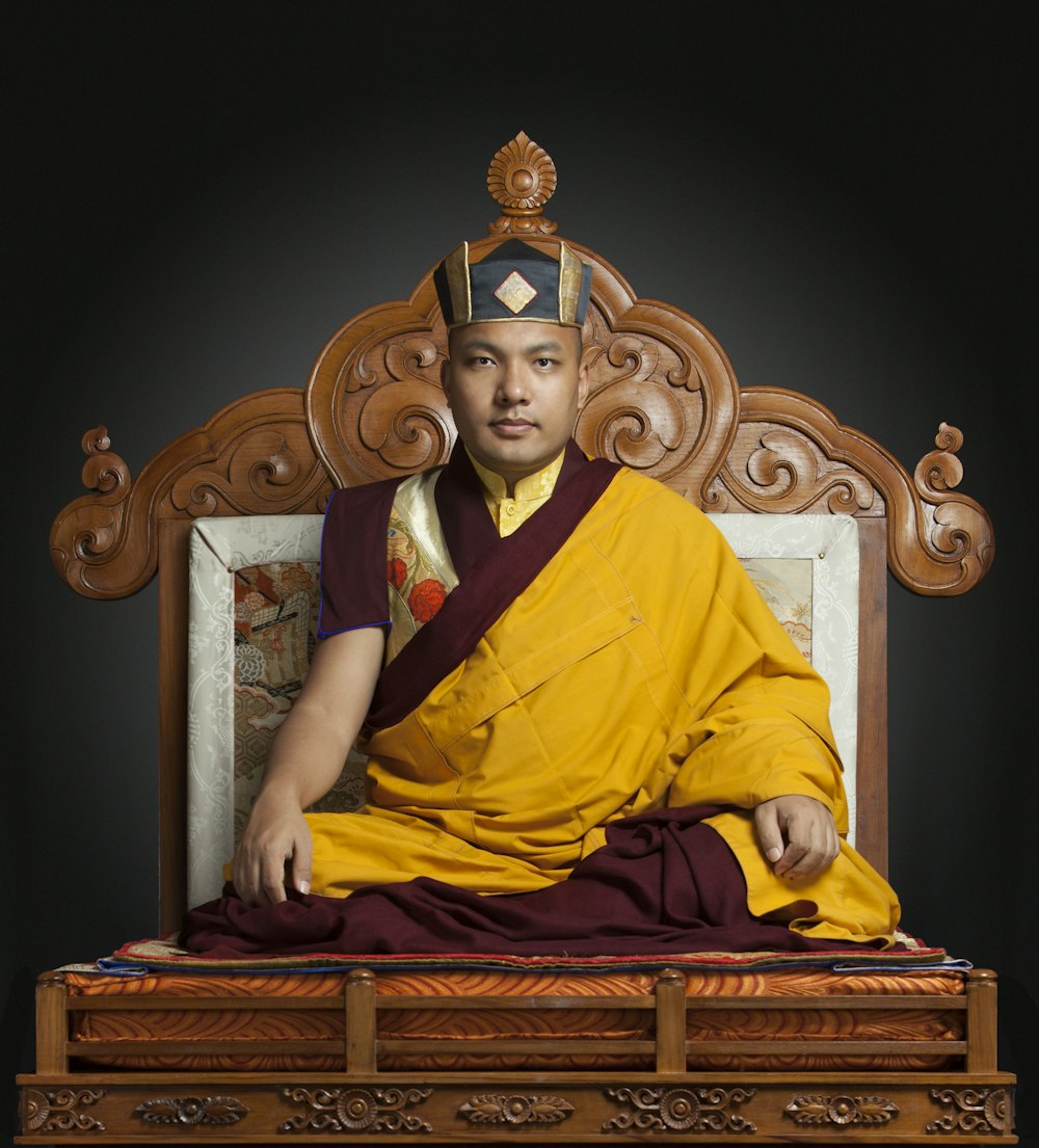 man in yellow and red robe sitting on brown wooden bench