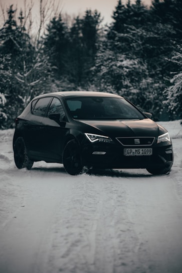 A sleek black sedan parked on a snowy road with the northern lights glowing softly in the sky above Kiruna.