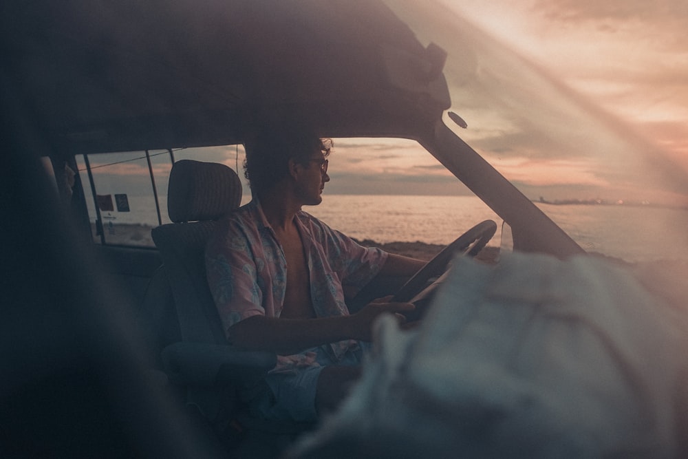 夕暮れ時に車のシートに座る青いボタンアップシャツを着た男性