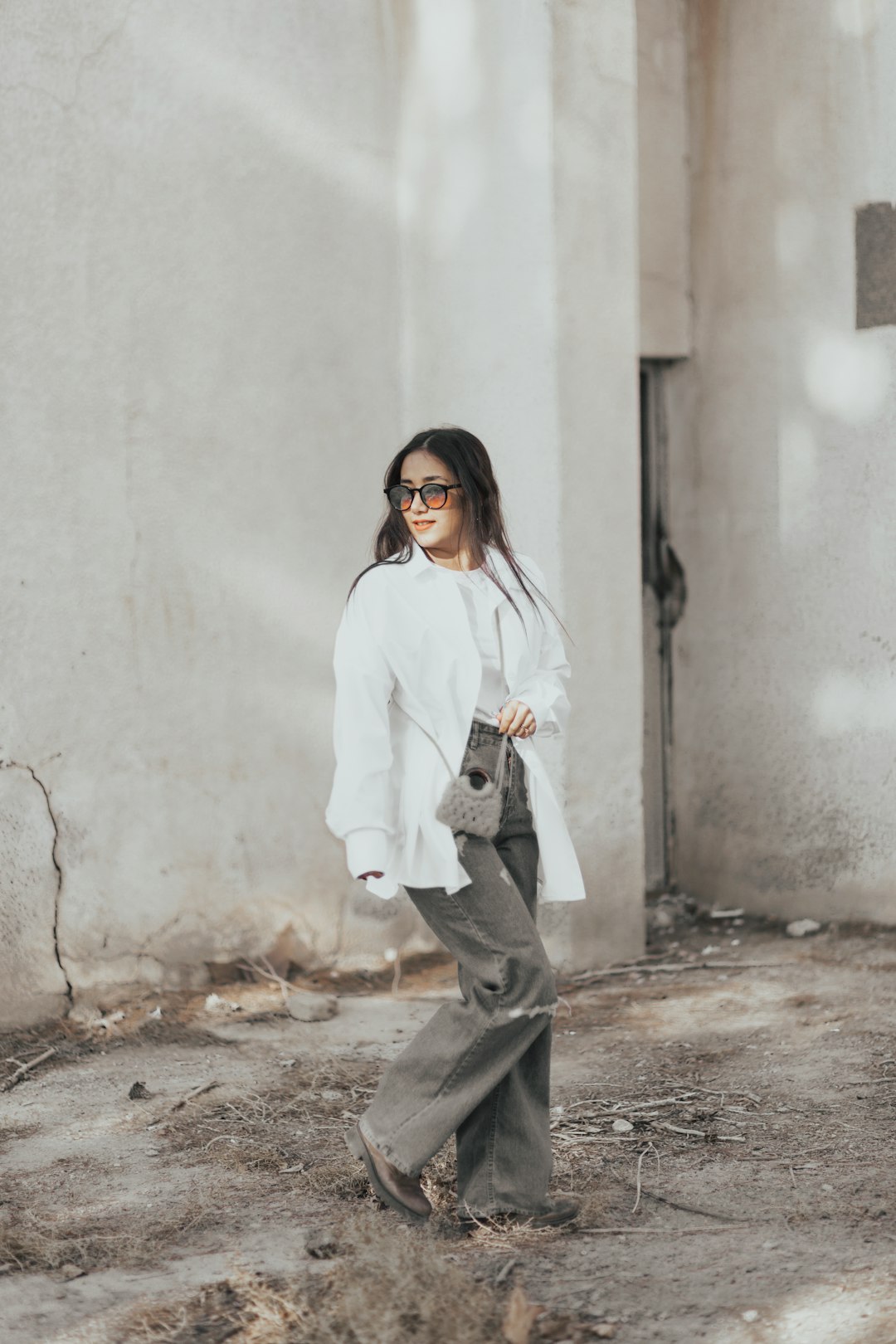 woman in white long sleeve shirt and gray pants standing beside white wall