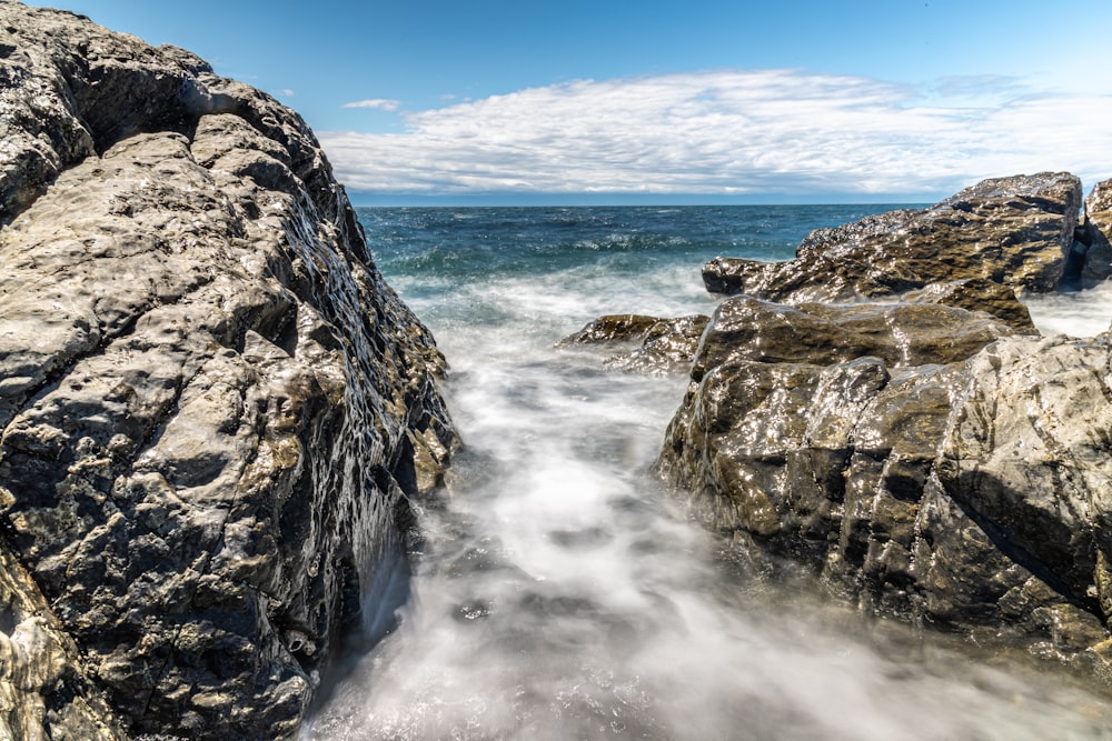 rocky shore with ocean waves crashing on rocks under blue sky during daytime