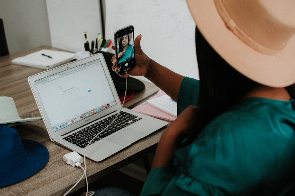 person holding black smartphone near macbook pro