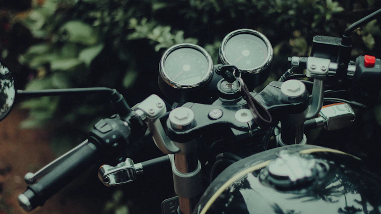 A sleek GPS tracking device installed on a motorcycle dashboard with a blurred forest background.
