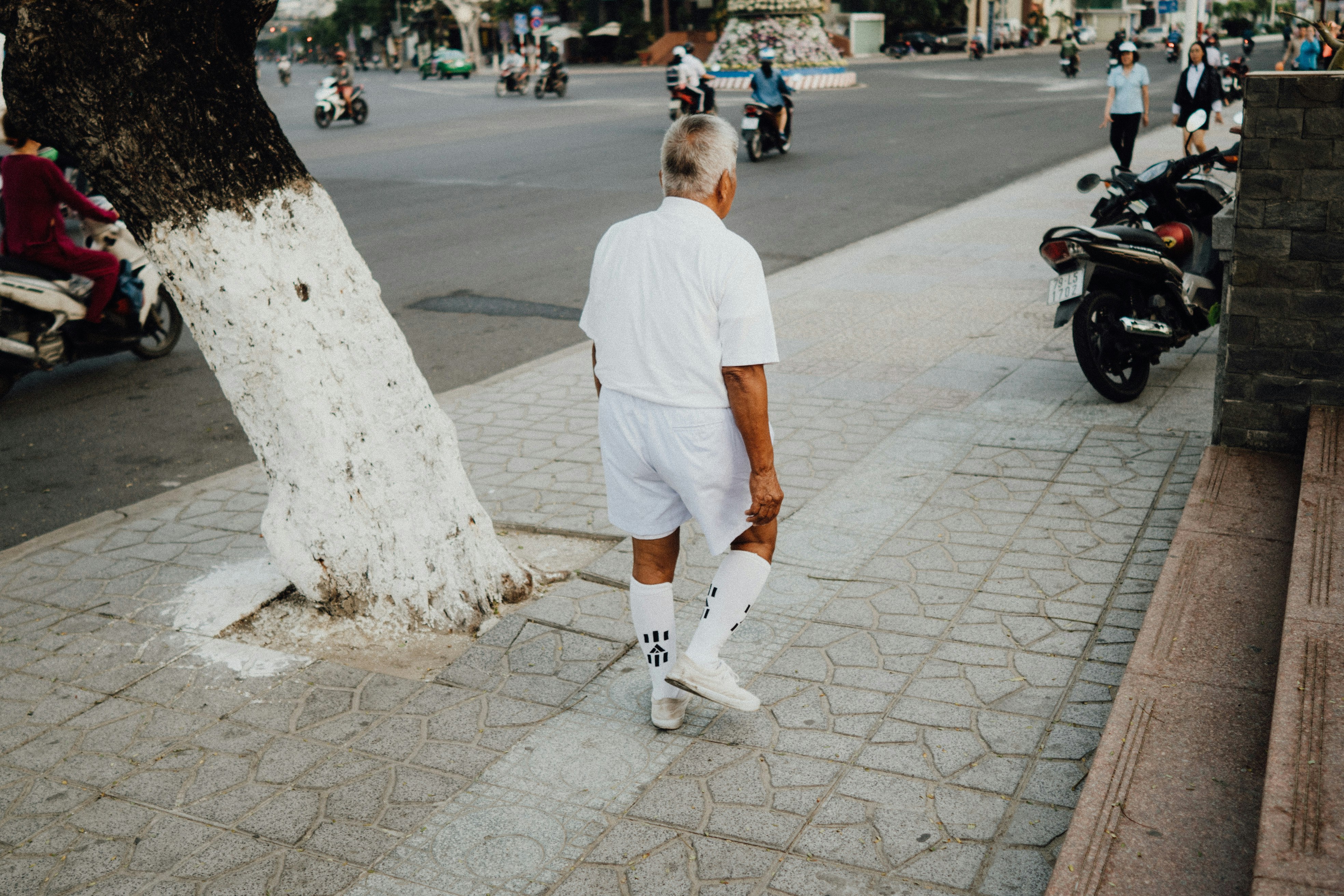 man in white t-shirt walking on sidewalk during daytime