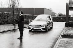 man in black jacket standing beside silver mercedes benz car