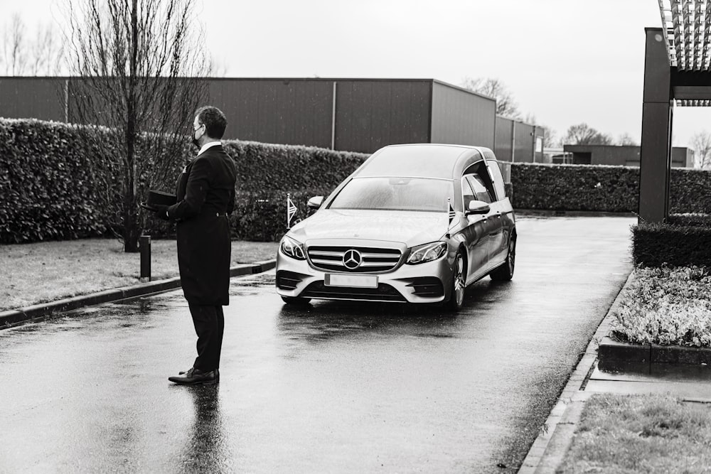 Uomo in giacca nera in piedi accanto all'auto d'argento del benz di Mercedes