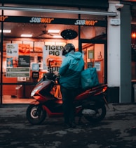 man in green jacket sitting on red and black motor scooter