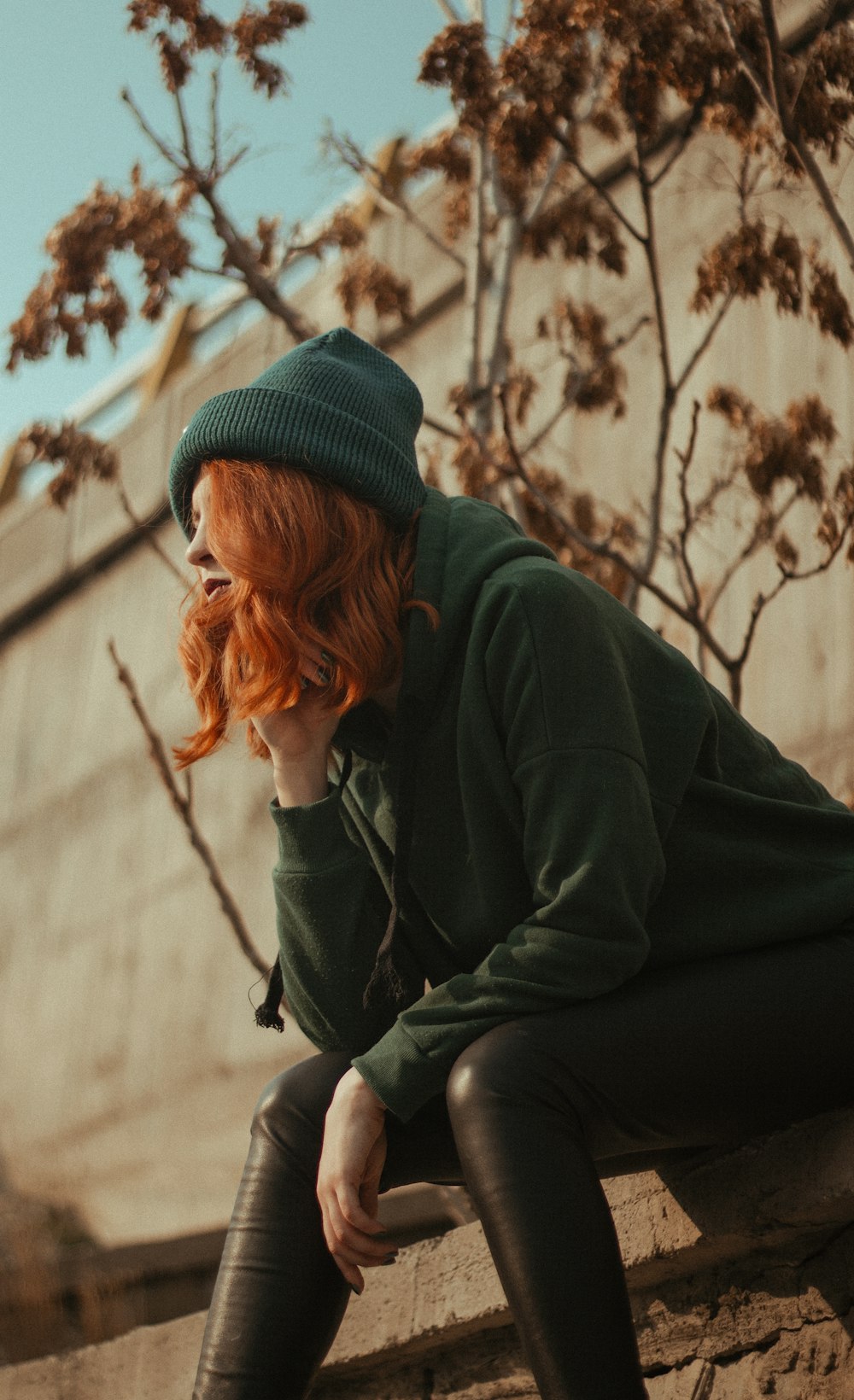 woman in green sweater and green knit cap sitting on brown wooden floor