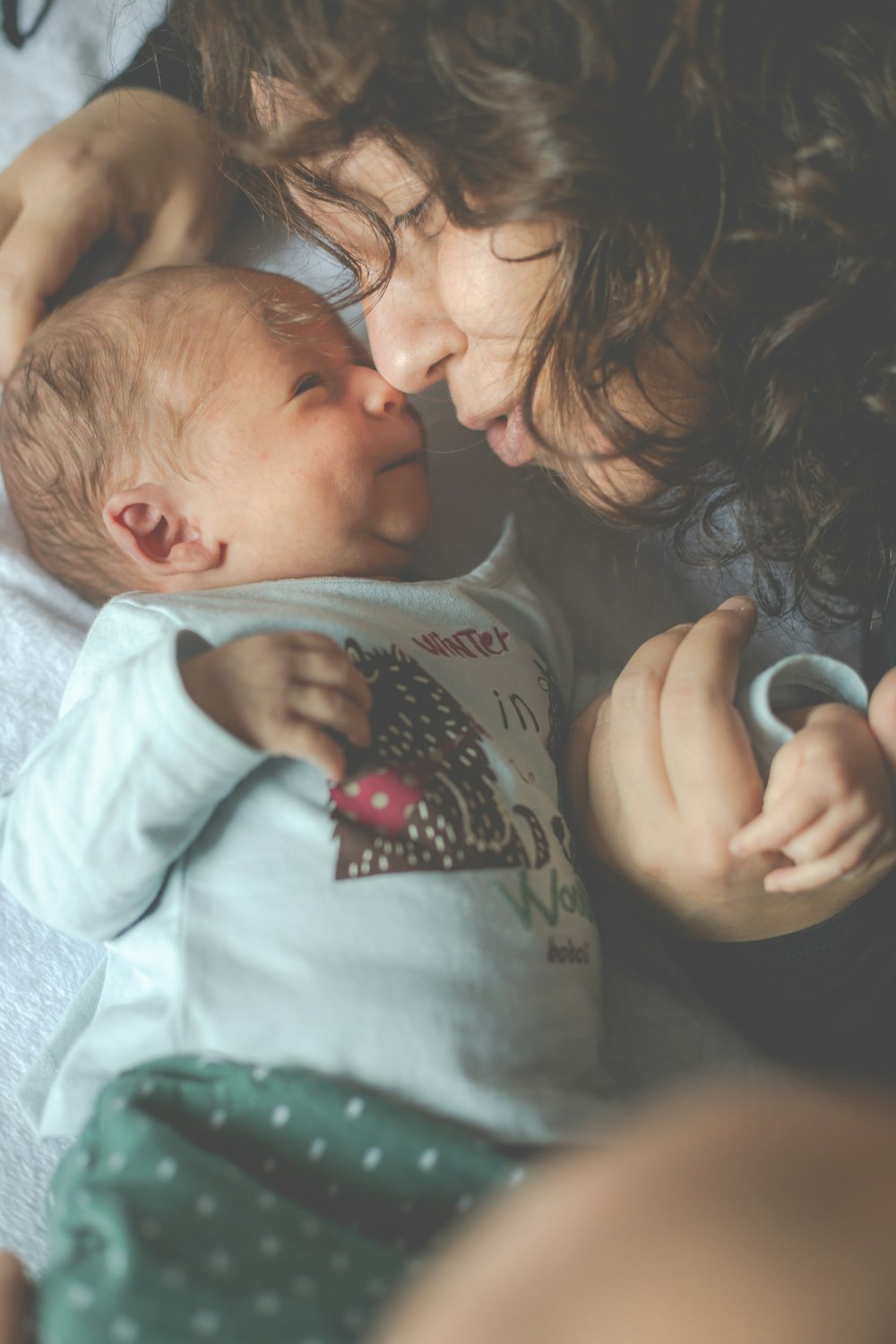 Femme en chemise grise à col rond à côté de bébé en grenouillère grise