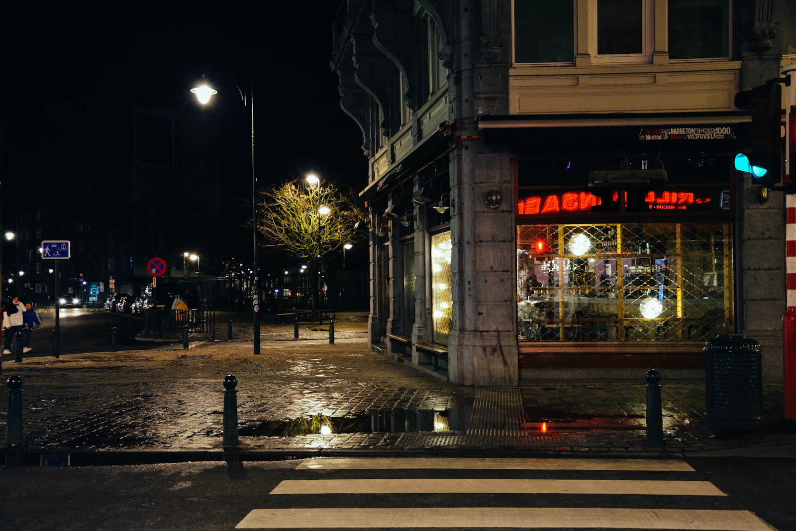 A lit street corner at night with people crossing