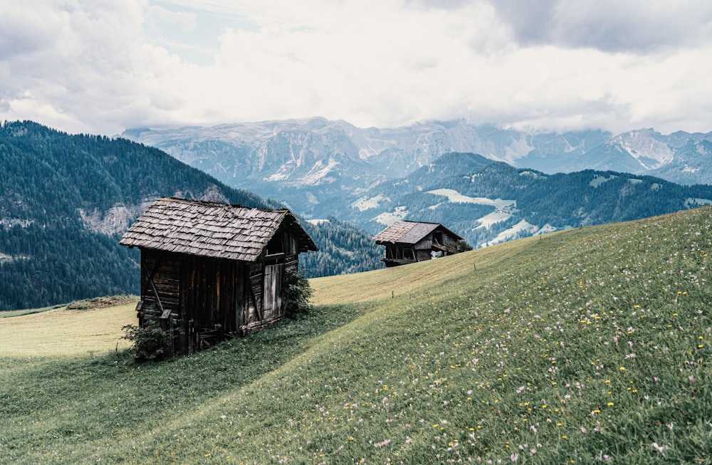 brown wooden house on green grass field near mountain under white clouds during daytime