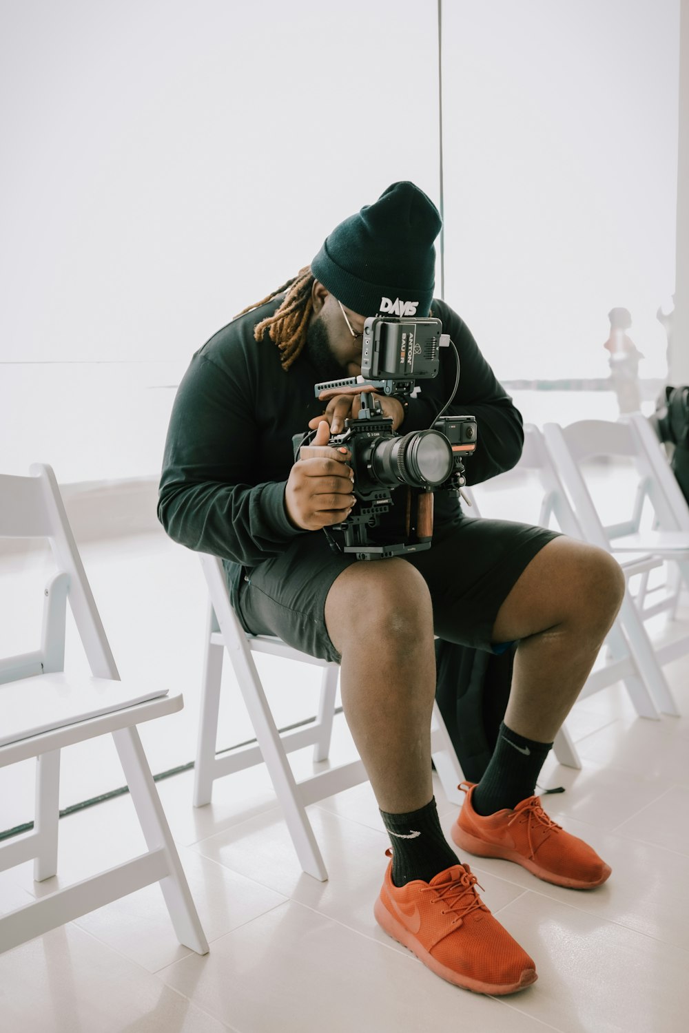 man in gray hoodie and black shorts sitting on white chair holding black dslr camera
