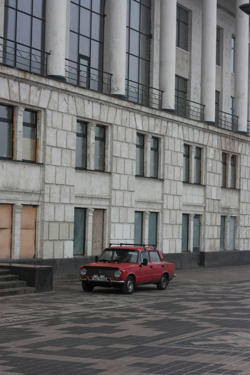 carro vermelho estacionado ao lado do edifício de concreto branco durante o dia