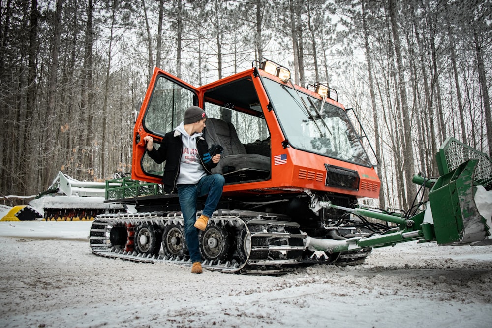 man in blue jacket and blue denim jeans sitting on orange and black heavy equipment