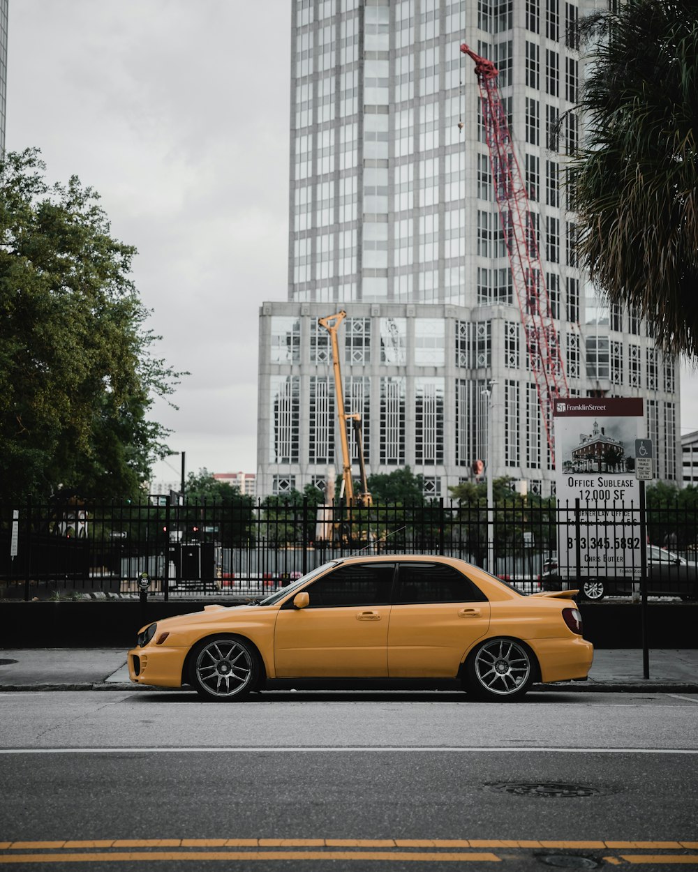 yellow sedan on road near white high rise building during daytime