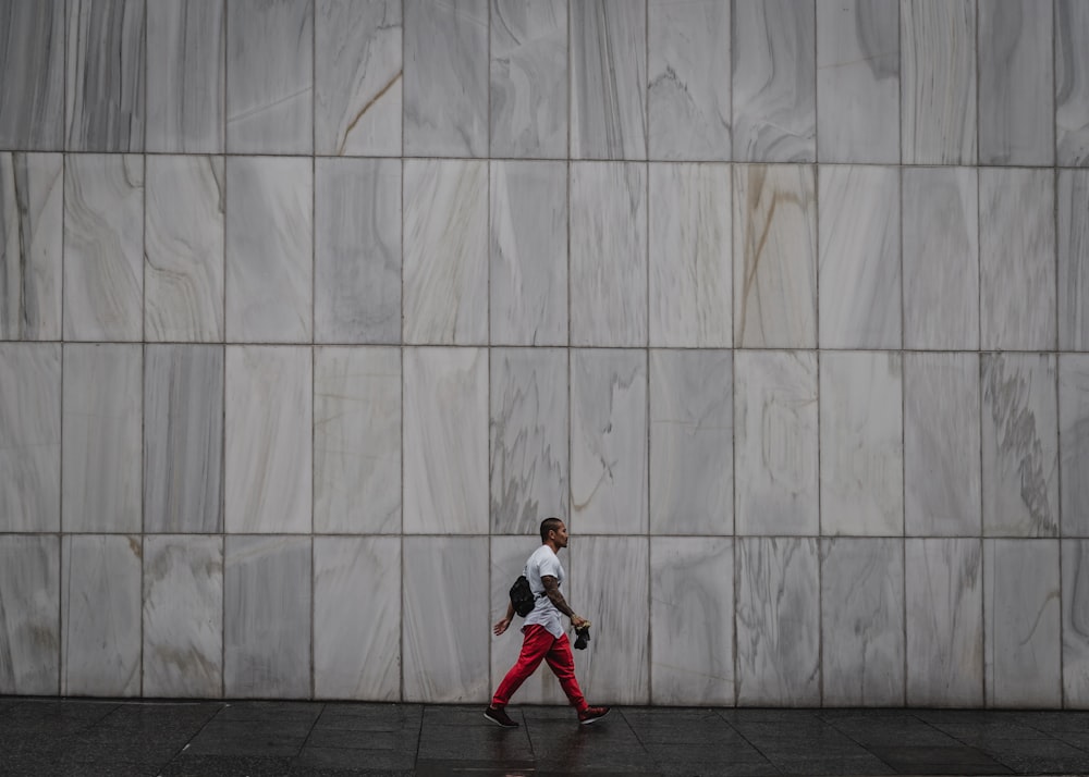 girl in white long sleeve shirt and red pants standing beside white wall