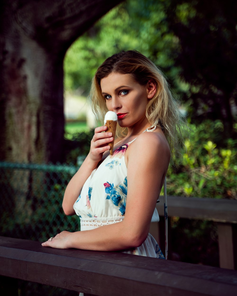 woman in white and blue floral sleeveless dress sitting on brown wooden bench