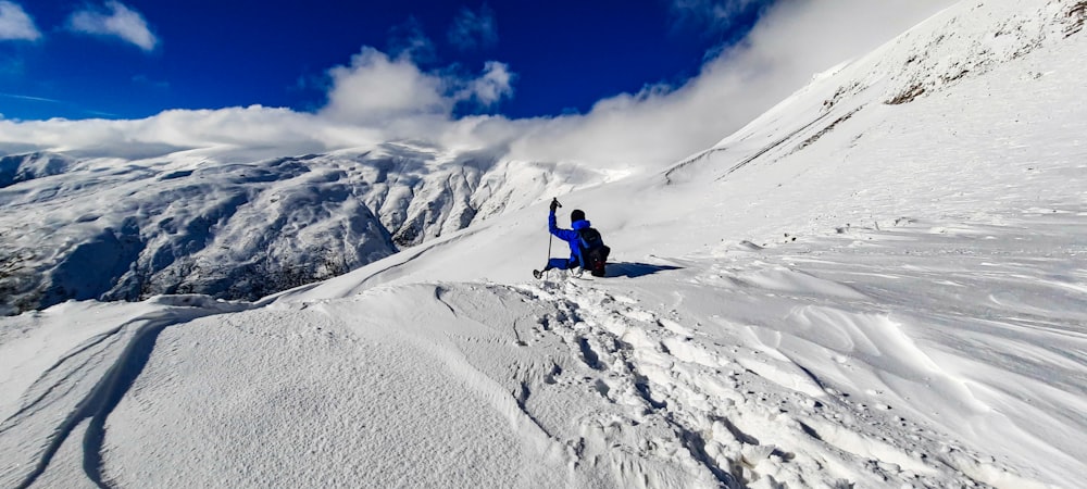 person in blue jacket and black pants sitting on snow covered mountain under blue sky during