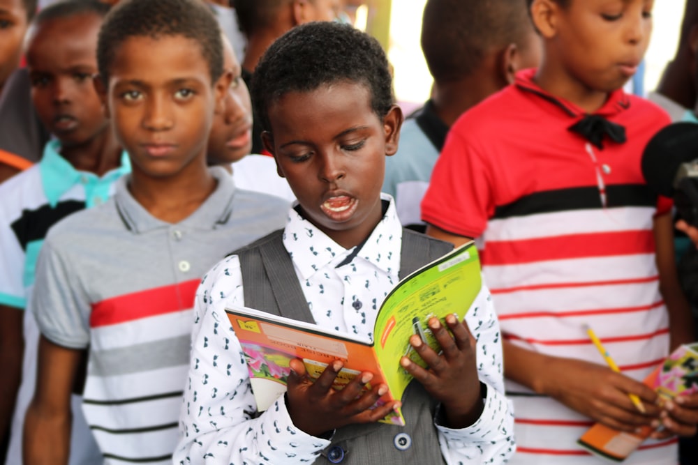 Homme en polo rouge et blanc tenant un livre jaune