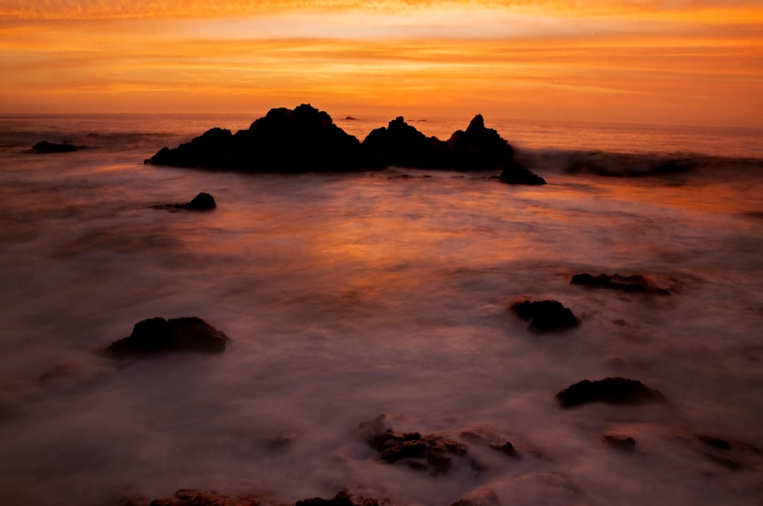 silhouette of rock formation on sea during sunset
