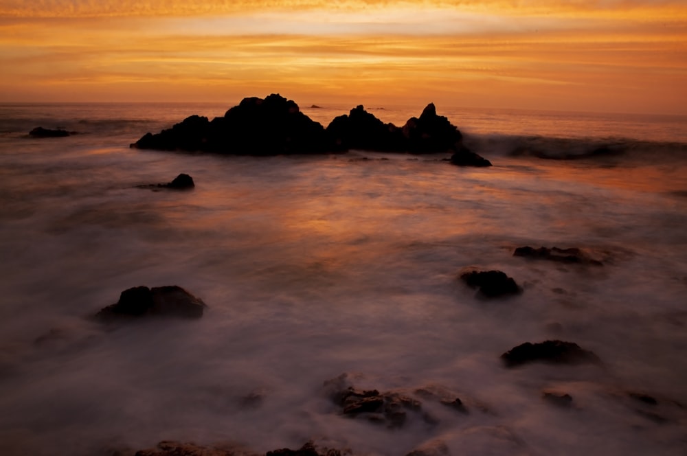 silhouette of rock formation on sea during sunset