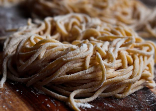 Close-up photo of fresh hand-rolled noodles on a wooden board in a traditional kitchen.