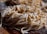 A close-up view of a pile of fresh, uncooked pasta noodles, sprinkled with flour. The image highlights the texture and details of the noodles, which appear to be homemade. The background is slightly blurred, emphasizing the focus on the pasta.