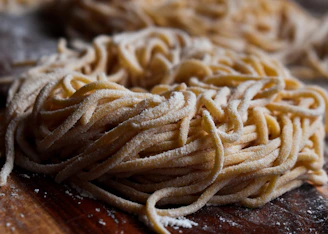 Close-up of golden fresh pasta strands gently dusted with flour on a rustic wooden board.