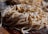 A close-up view of a pile of fresh, uncooked pasta noodles, sprinkled with flour. The image highlights the texture and details of the noodles, which appear to be homemade. The background is slightly blurred, emphasizing the focus on the pasta.