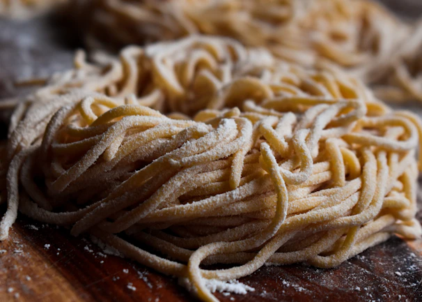 Close-up of golden fresh pasta strands gently dusted with flour on a rustic wooden board.