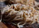 Close-up of a rustic wooden bowl filled with golden fresh pasta strands dusted with flour.