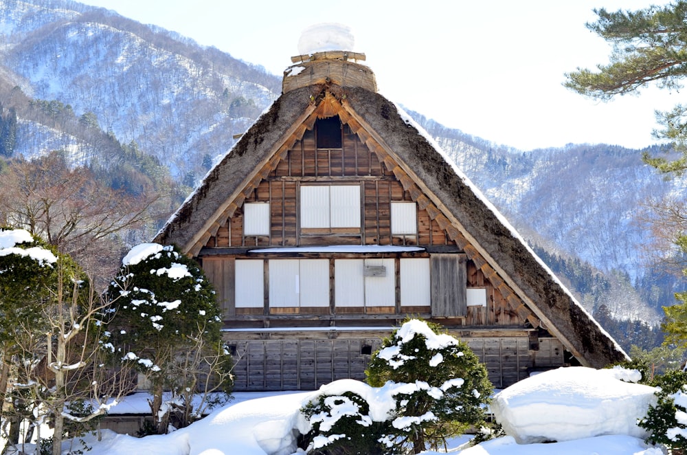 brown wooden house covered with snow near snow covered mountain during daytime