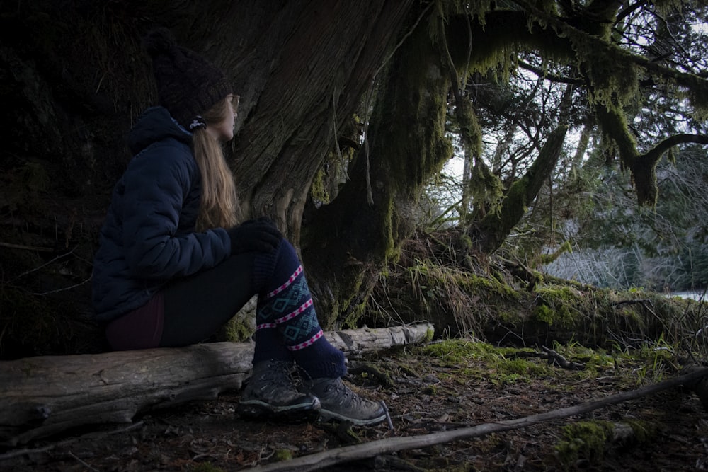 woman in blue jacket sitting on brown wooden log